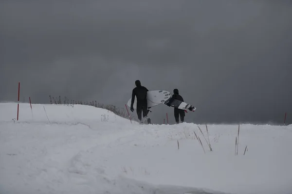 ノルウェーの海でサーフィンした後に雪のビーチで実行されている本物の地元の北極サーファー 雪の冬に山の背景をかぶった ノルウェーのロフテン島 ノルウェーの海岸線 冬の水活動 極端なスポーツ — ストック写真