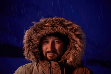 Kışın fırtınalı bir gecede sıcak kürk ceket giyen bir adam.