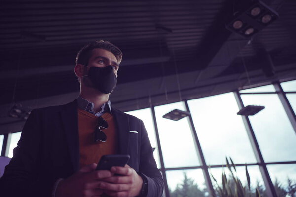 Business man wearing coronavirus protective medical face mask while using smartphone and new normal smart technology