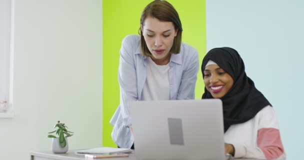 Mångfald Etniska kvinnor möts i ämbetet. Leende flicka i Hijab arbetar på laptop, blond tittar på skärmen. — Stockvideo