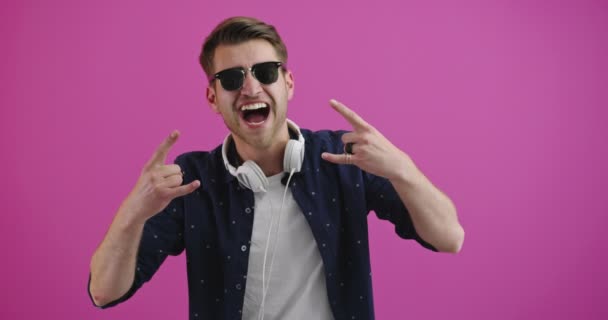 Νεαρός όμορφος άντρας που φοράει ακουστικά ακούγοντας μουσική πάνω από απομονωμένο φόντο χρώμα χορεύει και χαμογελά με τα χέρια σηκωμένα — Αρχείο Βίντεο