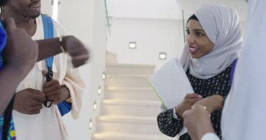Bir grup mutlu Afrikalı öğrenci sohbet ediyor ve takım buluşması yapıyor. Ev ödevi için birlikte çalışıyorlar. Geleneksel Müslüman başörtüsü giyen kızlar.