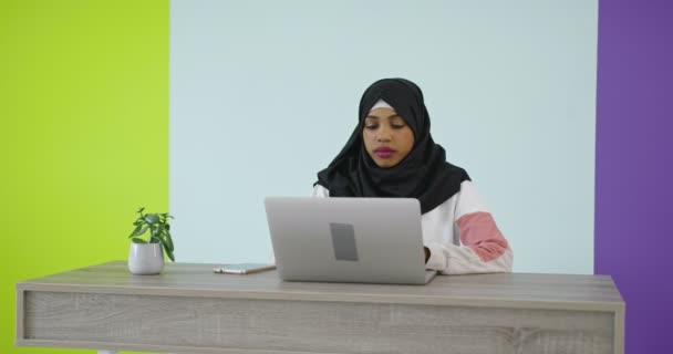 Mujer hermosa y feliz en pañuelo de cabeza de hijab usando teléfono móvil con computadora portátil en la oficina en casa. — Vídeo de stock