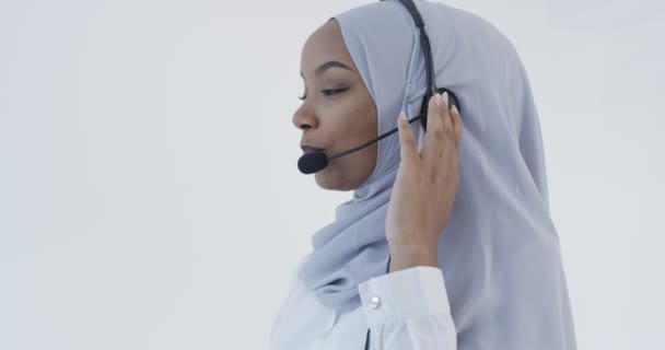 Mujer musulmana africana con bufanda de hijab representante del cliente mujer de negocios con auriculares telefónicos ayudando y apoyando en línea con el cliente en el moderno centro de llamadas brillante aislado sobre fondo blanco — Vídeos de Stock