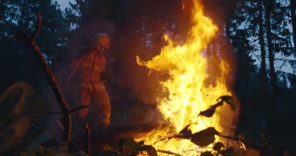 Bomberos saltando sobre fuego en bosque denso, bombero con equipo de seguridad y hacha extinguiendo fuego en el bosque por la noche — Vídeos de Stock