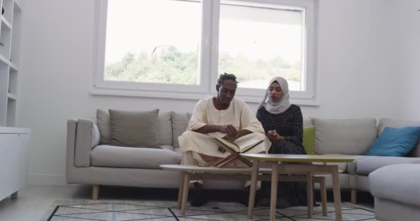ラマダーン月の自宅でアフリカ系イスラム教徒のカップルはソファの上の近代的なアパートでクルアーンホリーイスラム教の本を読んで — ストック動画