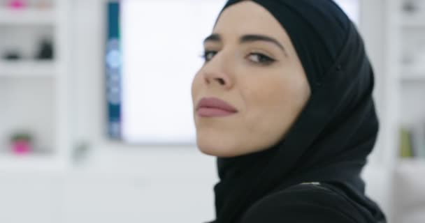 Portret van jonge moslim vrouw die islamitische hijab kleding draagt zittend op de bank TV kijkend — Stockvideo