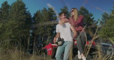 Genç hippi çift sabah off-road arabasında eğleniyor. Hippi kıyafetli bir çift gün doğumunu bekliyor ve eğleniyorlar.
