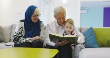 Geleneksel Müslüman aile büyükbabaları ve çocukları Kuran okuyup kanepede birlikte dua ediyorlar.