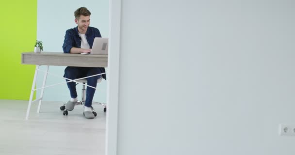 一个英俊的年轻人在一个现代化的办公室里用笔记本电脑，一个在家里工作的自由职业者 — 图库视频影像