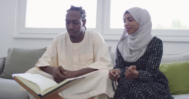 Африканская мусульманская пара дома в Рамадан чтение Корана Холли Ислам книги в современной квартире на диване — стоковое видео
