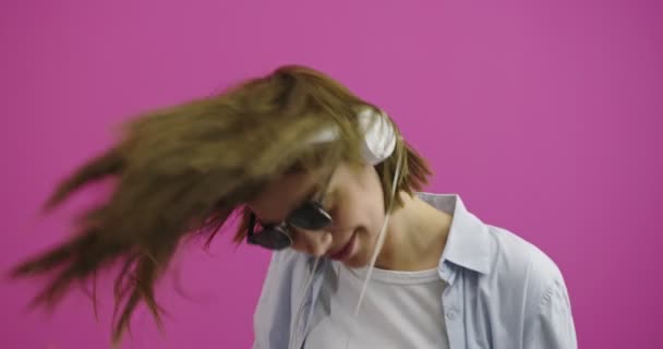 Wanita lucu memakai headphone mendengarkan musik dan menari di atas backgorund warna — Stok Video