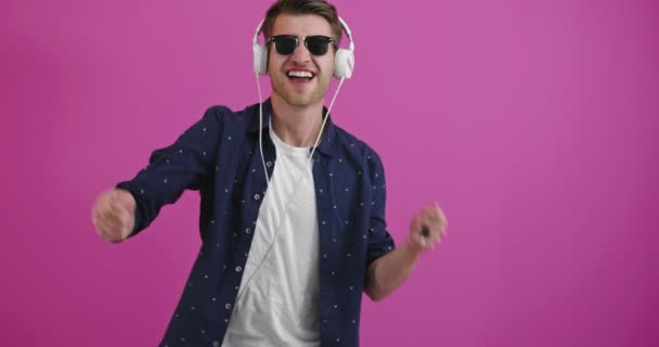 Jonge knappe man draagt koptelefoon luisteren naar muziek over geïsoleerde kleur achtergrond dansen en glimlachen met opgeheven armen — Stockvideo