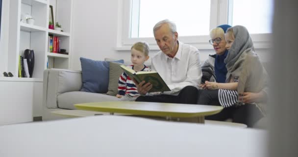 Família muçulmana tradicional avós com crianças lendo o Alcorão e orando juntos no sofá — Vídeo de Stock
