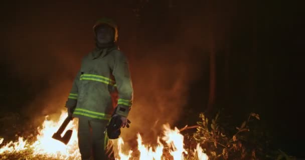 消防队员拿着全副武装，手里拿着斧头，站在一片火红的森林后面 — 图库视频影像