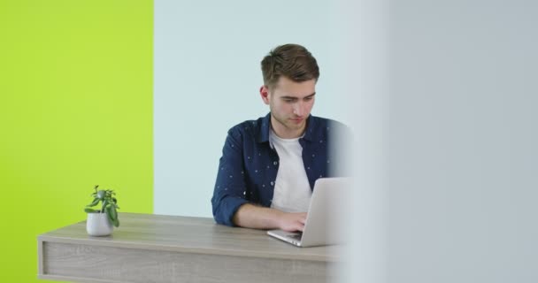一个英俊的年轻人在一个现代化的办公室里用笔记本电脑，一个在家里工作的自由职业者 — 图库视频影像