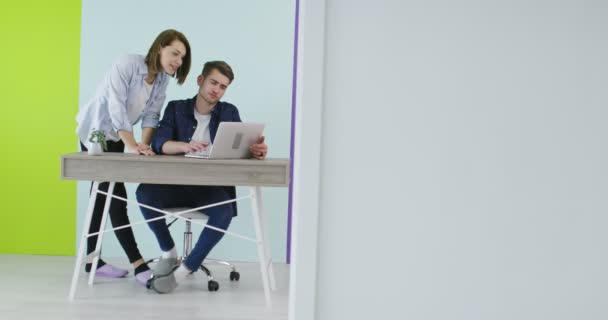 Positiv smilende mand og kvinde nær arbejdspladsen med laptop samarbejder i kontor – Stock-video