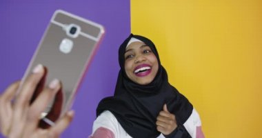 Cep telefonuyla tesettürlü mutlu Arap kadın renk arkaplanı üzerinde selfie çekiyor