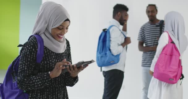 伝統的なイスラム教のヒジャーブの服を着て、タブレットを使用して背景に友人のグループと映画の学生 — ストック動画