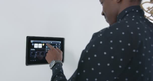 Чернокожий афроамериканец использует систему управления домом на стене для приложения "умный дом" — стоковое видео