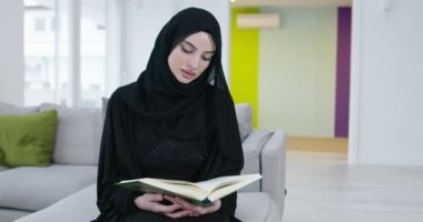 Geleneksel Müslüman kadın, iftar yemeğinden önce evde ramazan ziyafeti sırasında kanepede Kur 'an okuyor.