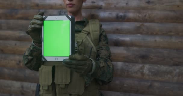 Soldatin der Armee zeigt einen Tablet-Computer mit einem leeren grünen Bildschirm über einem hölzernen Backgorund — Stockvideo