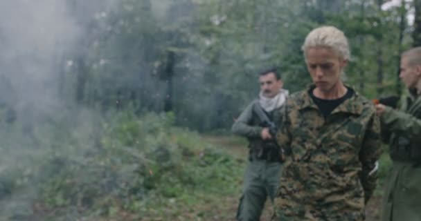 Терористи зі зброєю захопили жінку-солдата в щільному лісі з димом на задньому плані — стокове відео