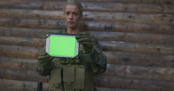 Kobieta żołnierz armii pokazuje tablet z pustym zielonym ekranie na drewnianym backgorund — Wideo stockowe