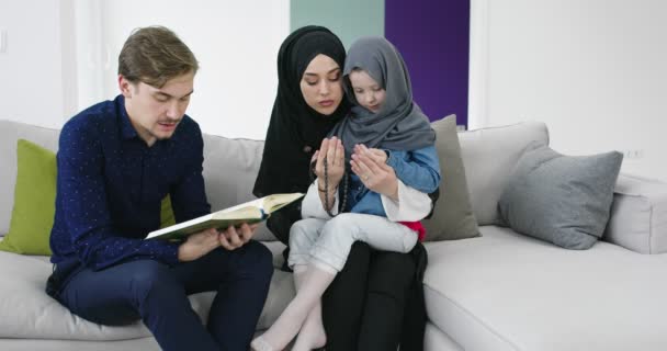Tradycyjni muzułmańscy rodzice z dziećmi czytający Koran i modlący się razem na kanapie przed iftarną kolacją podczas Ramadanu w domu — Wideo stockowe