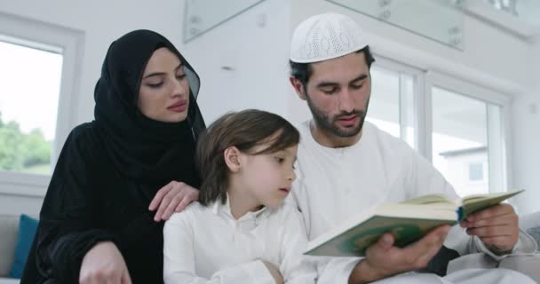 子供を持つ伝統的なイスラム教徒の家族はクルアーンを読み、自宅でラマダーンのごちそうの間にイフタールディナーの前にソファで一緒に祈る — ストック動画