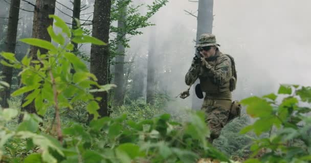 Στρατιώτης που κινείται μέσα σε δάσος καπνιστών με τουφέκι έτοιμο να πυροβολήσει, τρέχοντας μέσα στο δάσος κατά τη διάρκεια στρατιωτικής δράσης — Αρχείο Βίντεο