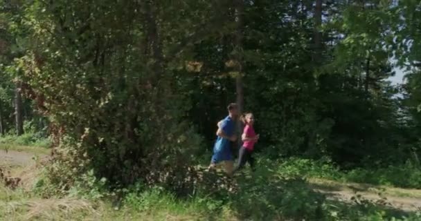Молода щаслива пара насолоджується здоровим способом життя під час бігу по сільській дорозі через красивий сонячний ліс, фізичні вправи та концепція фітнесу — стокове відео