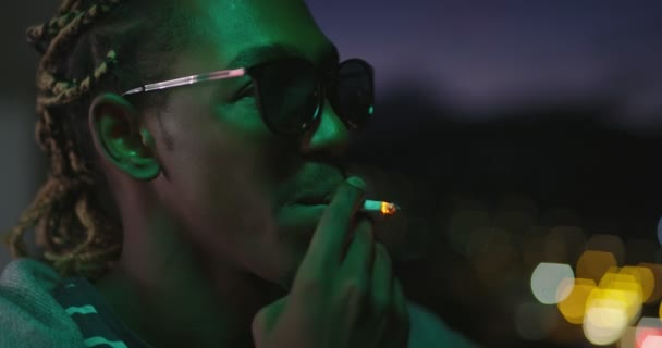 Afro amerikansk man som har fest dricka och röka med stadens ljus i bakgrunden med neonljus — Stockvideo