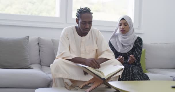 Африканская мусульманская пара дома в Рамадан чтение Корана Холли Ислам книги в современной квартире на диване — стоковое видео