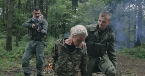 Terroristen met wapen gevangen vrouw soldaat gegijzeld in dichte bos met rook in backgorund — Stockvideo