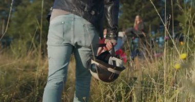 Hipster adamın hemlet tutup sabah güneşinde off-road arabasının yanında eğlenen bir arkadaş grubuna doğru gittiği yakın çekim.