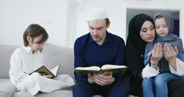 Tradycyjni muzułmańscy rodzice z dziećmi czytający Koran i modlący się razem na kanapie przed iftarną kolacją podczas Ramadanu w domu — Wideo stockowe