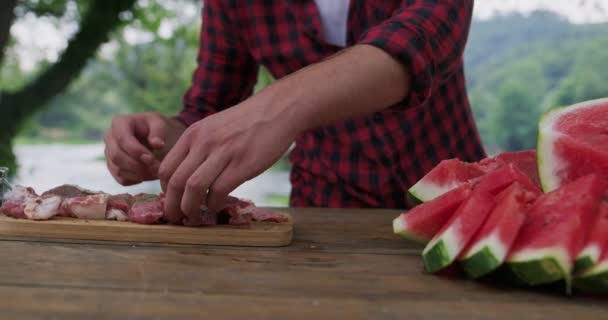 Man preparing meat and puting spices for barbeque and dinner beside river, preparing for dinner in nature in summer kitchen — Stock Video