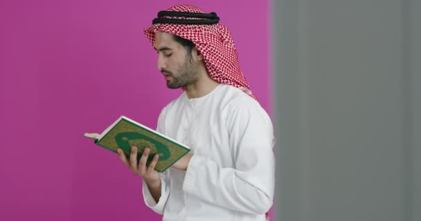 Jovem muçulmano árabe homem em roupas tradicionais orando no tapete na frente da parede rosa antes do jantar iftar durante uma festa ramadã em casa — Vídeo de Stock