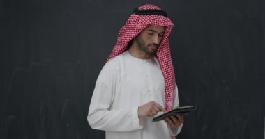 Siyah karatahta tabletinin önünde geleneksel giysiler içinde genç Arap adamın portresi. 