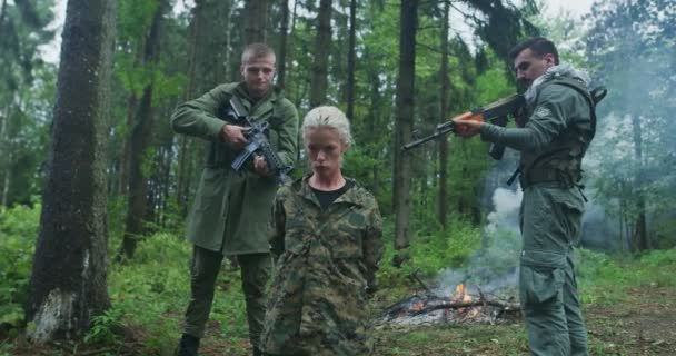 Террористы с оружием захватили женщину-солдата в заложники в густом лесу с дымом в заднем дворе — стоковое видео