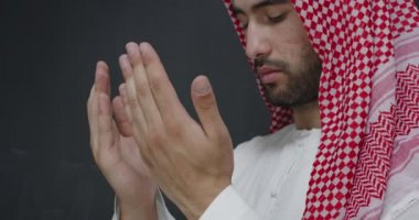 Geleneksel giysiler içindeki genç Arap adam Tanrı 'ya dua ediyor. Siyah karatahtanın önünde el ele dua ediyor.