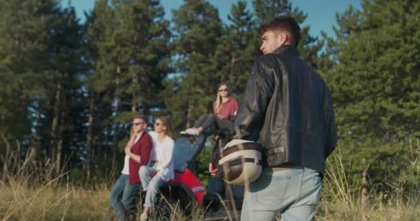 Närbild av hipster man som håller hampa och går mot grupp av vän som har kul i morgonsolen bredvid off road bil — Stockvideo