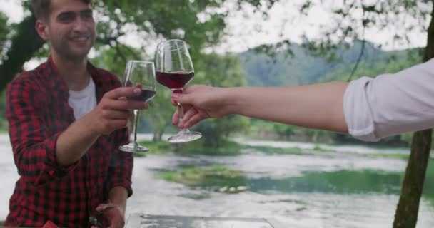Jeune couple heureux cuisine barbecue et toasts verre de vin rouge tout en ayant pique-nique dîner français en plein air pendant les vacances d'été près de la rivière à la belle nature — Video