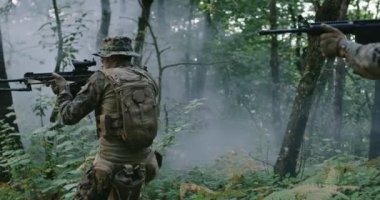 Ateş ve dumanlı ormanda tüfekle ilerleyen asker ateş etmeye hazır, askeri harekat sırasında ormanda koşuyor.