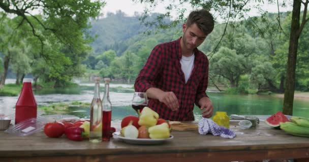 Homem preparando carne e colocando especiarias para churrasco e jantar ao lado do rio, preparando-se para jantar na natureza na cozinha de verão — Vídeo de Stock