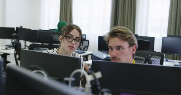 Başlangıç ofisinde iki genç iş arkadaşı bilgisayar kullanıyor ve birlikte konuşuyorlar. — Stok video