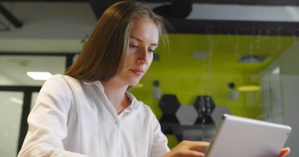 Hermosa chica joven con el pelo largo celebración tableta digital de lectura de correo electrónico en el sofá en la oficina de inicio — Vídeos de Stock