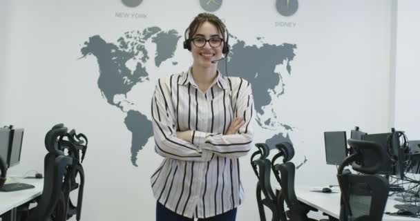 Piękny młody operator kobieta stoi i nosi słuchawki w jasnej przestrzeni biurowej — Wideo stockowe
