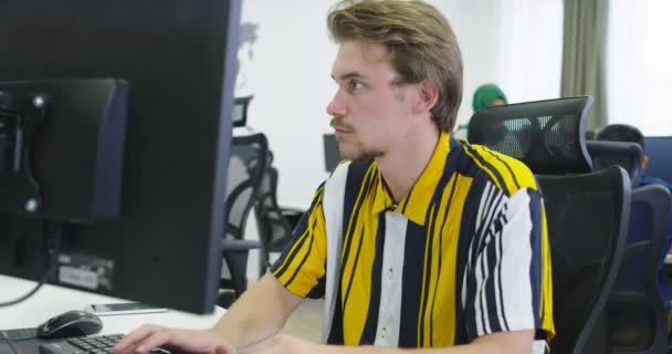 Masaüstü bilgisayarında çalışan yakışıklı genç işadamı başlangıç ofisinde masasında oturuyor. — Stok video